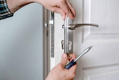 Door lock installation, repair, or replacement service. Door hardware installer locksmith working with open white door indoor. Hands of the master close-up