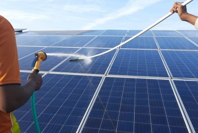 Two men cleaning solar panels (modules) using water and wiper. Applying forced water jet.
